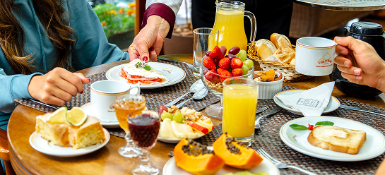 Mesa de café da manhã ou chá da tarde com frutas, bolos e bebidas sendo servida a hóspedes na Pousada D'Biagy Raízes