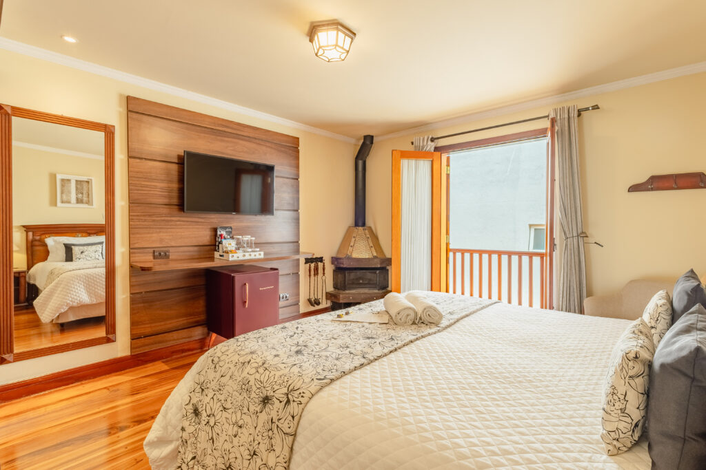 Quarto da Suíte Luxo com Lareira na Pousada D'Biagy Raízes, cama queen, Smart TV e acesso à sacada com vista