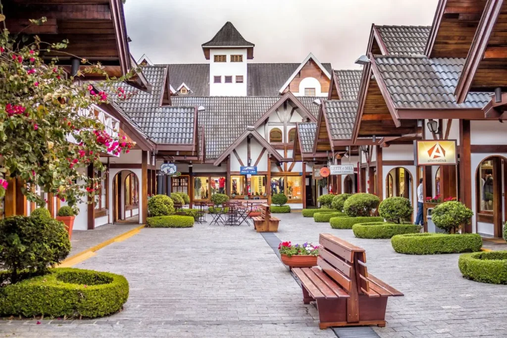 Portal de entrada de Campos do Jordão com arquitetura alpina, paisagismo florido e céu azul, marcando a chegada à cidade serrana no interior de São Paulo.