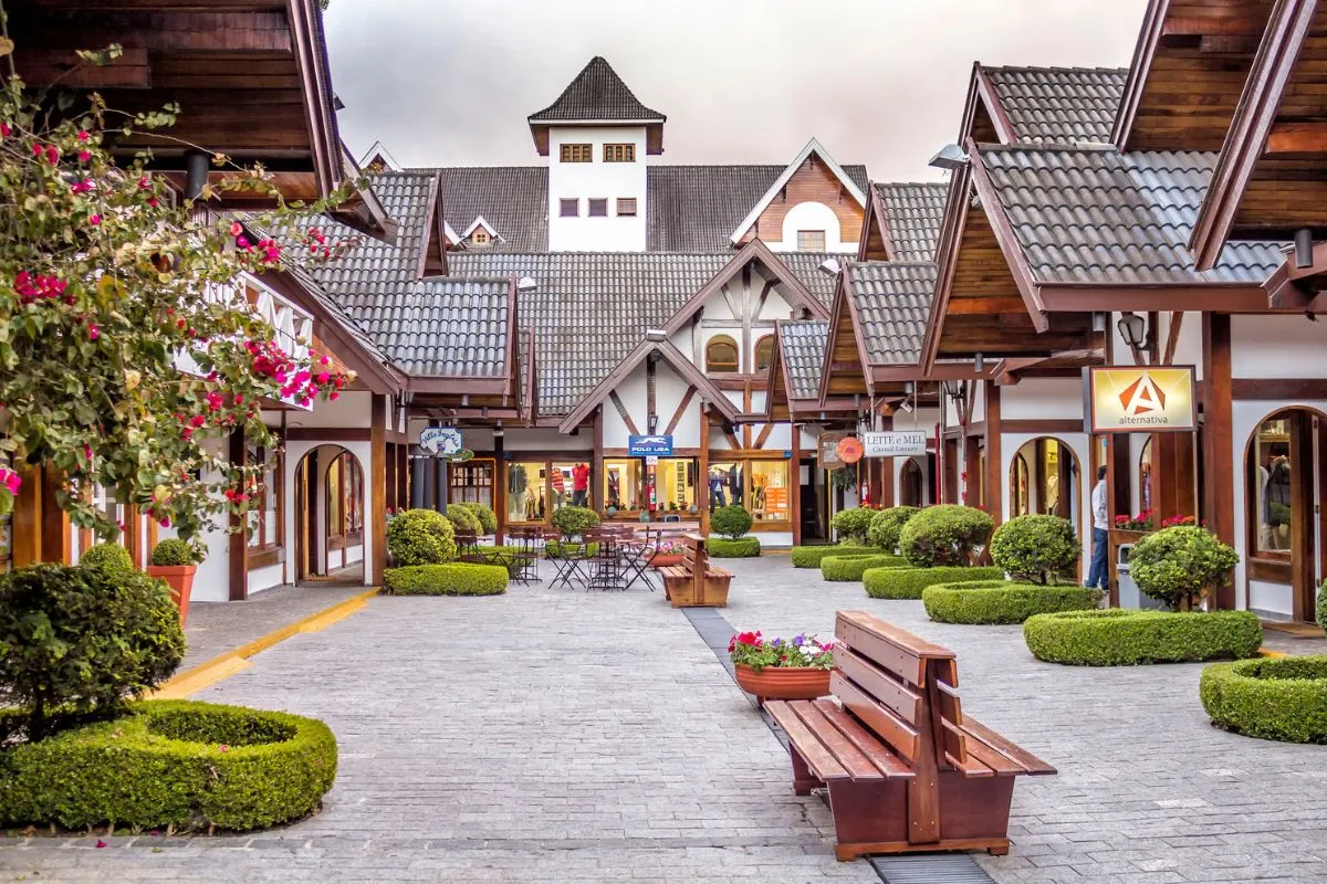 Portal de entrada de Campos do Jordão com arquitetura alpina, paisagismo florido e céu azul, marcando a chegada à cidade serrana no interior de São Paulo.