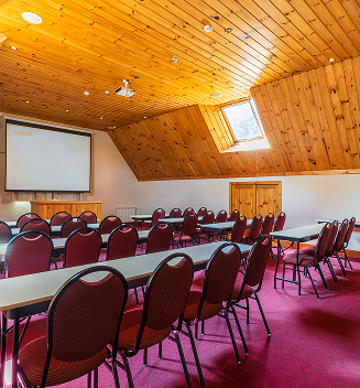 Salão de eventos da Pousada D'Biagy Premium com cadeiras, mesa e projetor, pronto para palestras e treinamentos.